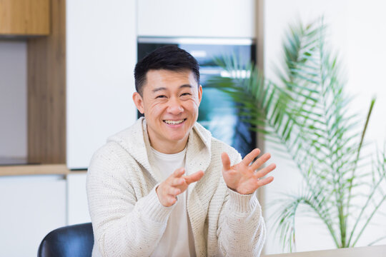 Asian Man Talking Online On Video Call At Home Room With Headset. Male In Casual Clothes Looking At Camera, Meeting Or Conference In Distance. Portrait Student Or Teacher Lecture Training. Webcam View