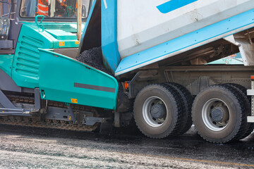 A truck is pouring hot asphalt into the bucket of an asphalt paver. Close-up, copy space. © Sergii
