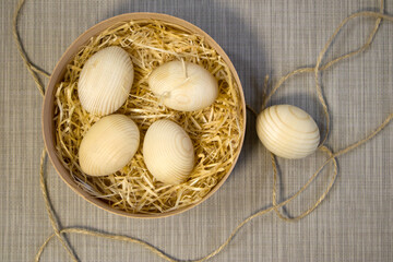 Easter wooden eggs, blanks for decor, painted in wooden basket with straw close-up on a plain linen background