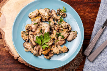 Peeled mussels in sauce on a dark wooden background.