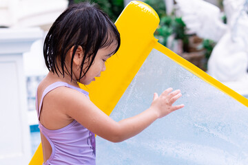Side view of pretty Asian child holding yellow rubber raft. Kid playing water in the pool. Summer day. Happy girl with holiday time. Children aged 4-5 years old.