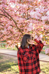 Outdoor portrait of young beautiful Caucasian teen girl smiling and looking into camera, blossom par full of cherry trees on a windy day. 4K footage with sunlight rays