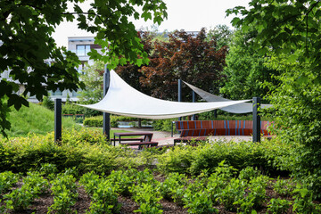Wooden seats in the park, sheltered from the sun by a canopy.