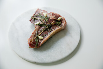 Raw rib eye, t-bone steak of beef on a board with a meat cleaver, onion and seasonings