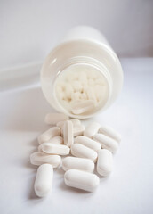 White medicinal pills are scattered from a White bottle container close-up