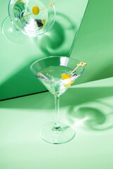 Glass of martini cocktail with green olives reflected in mirror. Focus on shadows