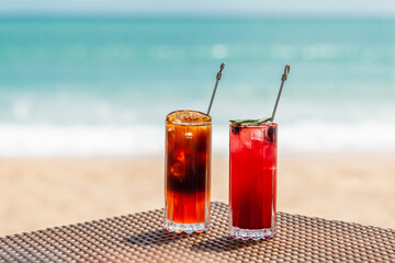 Fresh Cold Orange and Raspberry Cocktails on Table on Beach with Sunny Sea on Background. Fruit Mocktails in Beach Restaurant. Iced Healthy Colorful Drinks in Tropical Resort. Hotel Vacations Concept.