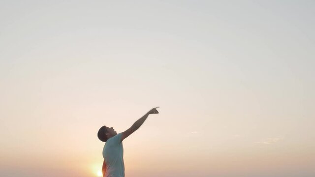 man in cheerful mood throwing paper airplane in field on sunset on background of clear sky, concept of active rest outdoors and relaxation, toy of childhood