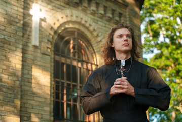 Christian priest with cross standing by the church.