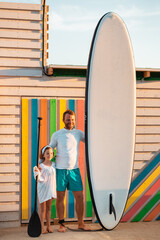 Summer holidays. Father and daughter posing with sup board. Man holding a sup board, and girl holds...
