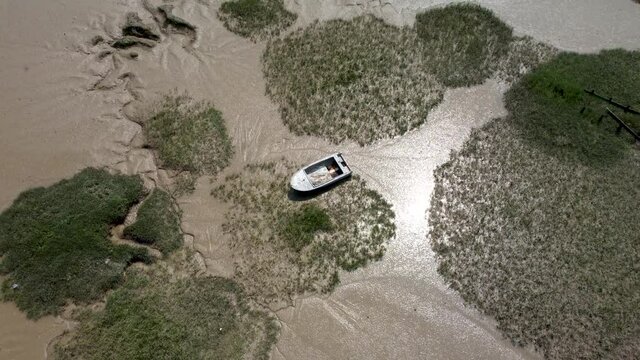 4K low and slow drone video over wet sand banks with a blue disowned boat