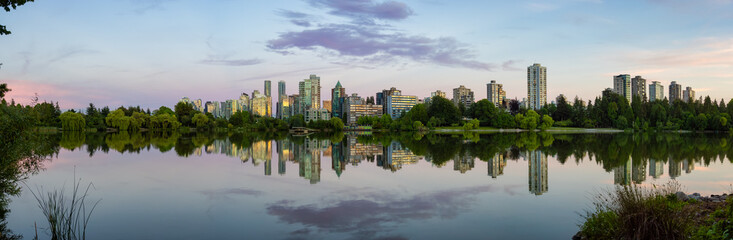 Panoramic View of Lost Lagoon in famous Stanley Park in a modern city with buildings skyline in background. Colorful Sunset Sky. Downtown Vancouver, British Columbia, Canada.