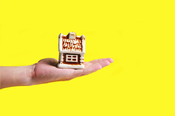 Toy house on palm of your hand on yellow background, mortgage sale or purchase of real estate, houses, apartments.