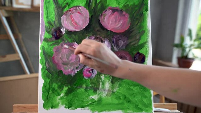 Close-up of a brush for painting the artist makes strokes of acrylic paint paints beautiful flowers peonies.creativity brush on canvas hobby art workshop
