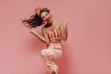 Positive girl with wavy long hair in bright modern top and pink stylish pants smiling and looking...