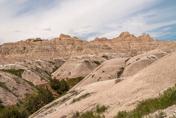 Badlands National Park, SD, USA - June 1, 2008: Green foliage grows in crevasse between beige geological deposits under dense blue cloudscape.