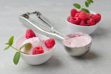 Homemade raspberry ice cream in a white cup on a light background. Stainless steel spoon for ice cream balls. Fresh raspberries with mint. Delicious and romantic dessert.