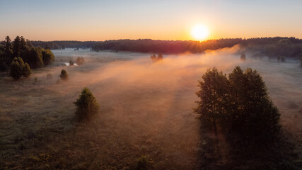 Gorgeous shot of fog in the countryside lit by first rays of the rising sun. Morning landscape of the valley