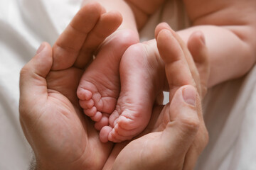 Father holding Baby Feet in Hands. Legs Newborn in male parents Hand. Small children's Feet in the Father's Palm. Close-up. Little Toes of Child and Man Hands of Happy Parent. Father's Day Holiday