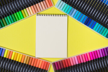 Colored felt-tip pens and a notebook on a yellow background with a place for text top view. Bright...