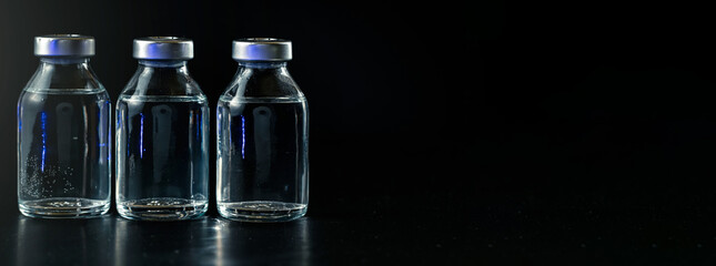 Three clear vaccine bottles with no labels with black background, space for text right side
