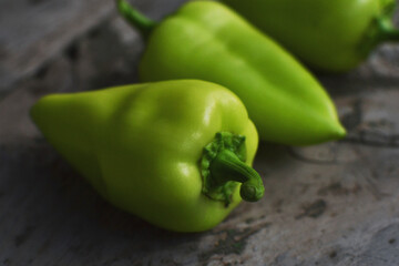 Three green ripe peppers lie on gray wooden surface, side view, copy space.