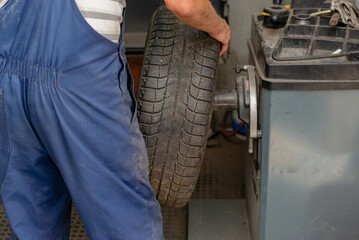 Car mechanic balancing car wheel on a computer machine balancer in auto repair service.