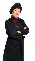 woman chef in black uniform. apron, shirt, hat. an elderly lady is a food preparation specialist. the lady stands straight and looks at us, crossed her arms on her chest. white background, isolated