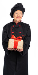 woman chef in black uniform. apron, shirt, hat. An elderly woman holds a gift wrapping with a red bow, a gift in a box in her hands. white background isolated