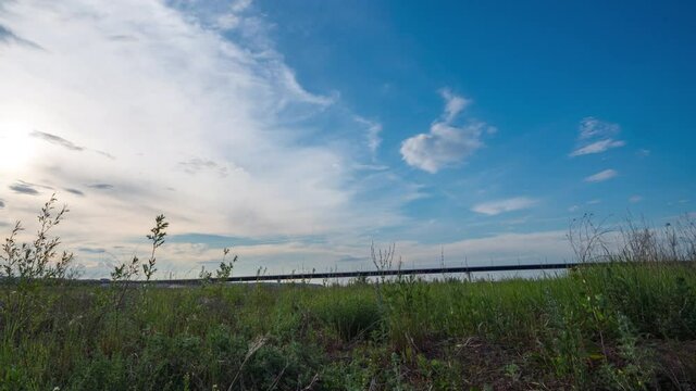 Time lapse of movement of white clouds across the blye sky. Sunset, in the evening. The movement of the camera in the grass above the river. 4K Hyperlapse