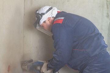 The worker cuts through the holes in the wall with a grinder for laying an electric cable to an electrical outlet
