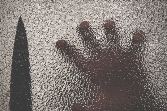 Knife in hand. Aggressive tin attack. Hacking attempt. The criminal behind the glass. Agony crooked hand. Criminal and victim, resisting the hands of the victim and attacking hand with a knife