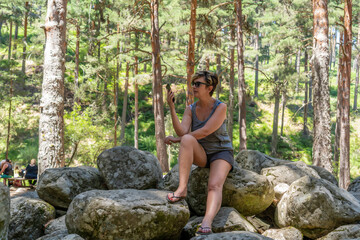 mujer haciendo una videollamada y selfies encima de unas rocas en la montaña rodeada de arboles