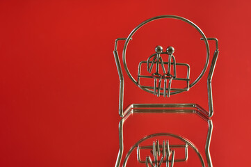 Beautiful closeup view of metal souvenir of couple sitting on a bench or swing on red reflective background. Love and affection concept. Copy space