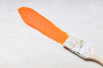 a brush with white bristles leaves an orange trace of paint