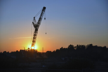 Obraz premium Industrial construction crane against the backdrop of the setting sun.