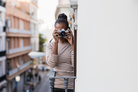 Cheerful black photographer with photo camera on balcony