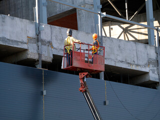 An aerial platform lifts workers to the upper floors of a building under construction. Background...