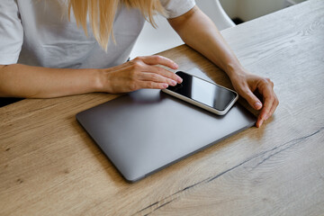 The girl sits at a table in front of a laptop and uses a smartphone for work. Remote work from home. Office desk with laptop and smartphone. Business background. Home office