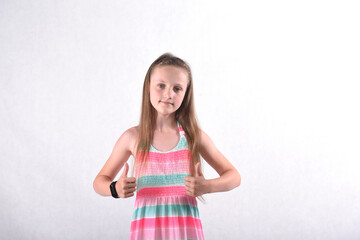 A beautiful school-age girl in the studio on a white background shows the gesture of fists with fingers with two hands as a symbol of positivity