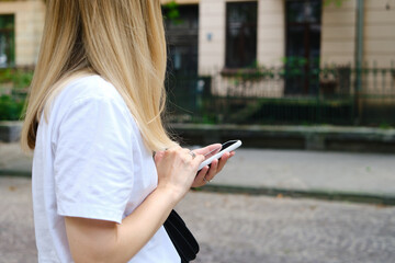 A girl on the street is holding a modern smartphone, sending a text message or using an application on her mobile phone. View city map using smartphone. Smartphone close-up