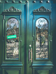 Antique green door with ornate details and sign with text - Open. Curved pattern metal gratings on double door of historic building