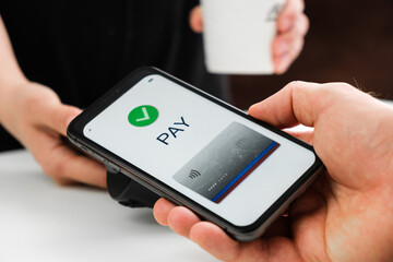 Close up man hand contactless paying for coffee by smartphone.