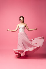 A young woman in a silk dress on a pink isoleted background. A model woman in a long evening dress...