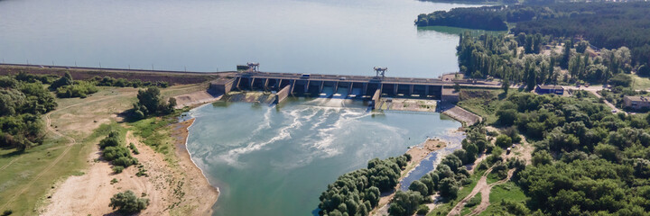Hydroelectric dam with flowing green water through gate, aerial view from drone. Panorama wide...