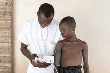 African male nurse measuring blood pressure to an African village kid with the help of a...