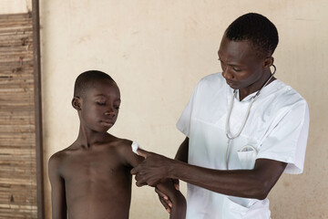 African young black boy after getting coronavirus vaccine. African doctor helping him with cotton...
