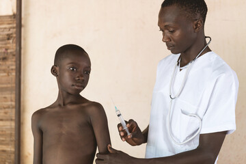 Little black African boy waiting to get his shot against coronavirus by a male black African doctor.