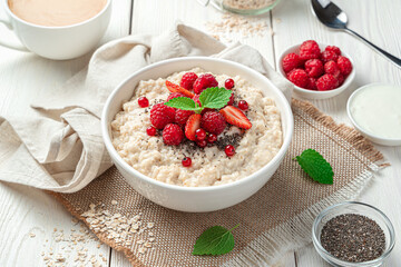 Oatmeal porridge with raspberries, strawberries, red currants and chia seeds on a light background.