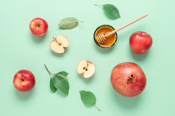 Rosh Hashanah. Apples, pomegranate and honey on a green pastel paper background. Jewish New Year. Traditional Jewish food. Top view, flat lay, copy space.